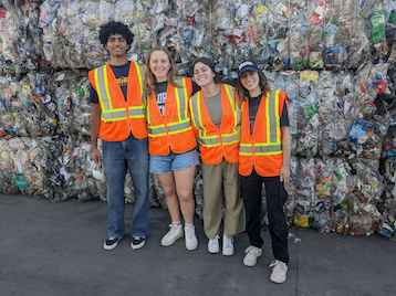 Student assistants posing in front of a pile of recycled material at EDCO's anaerobic digestion facility